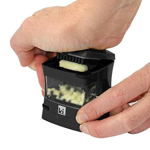 Hands using a black garlic chopper with chopped pieces visible.