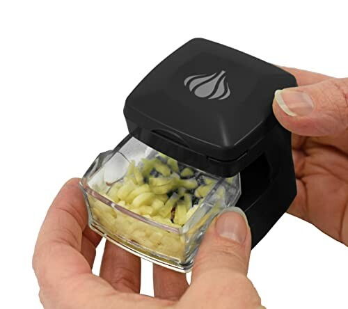 Hand using a garlic chopper with diced garlic inside.