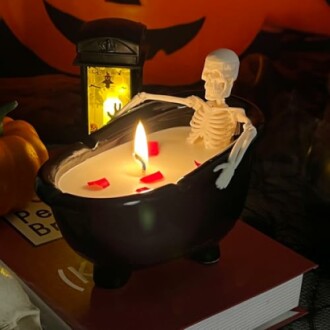 Skeleton in a cauldron-shaped candle with a flame, surrounded by Halloween decor.