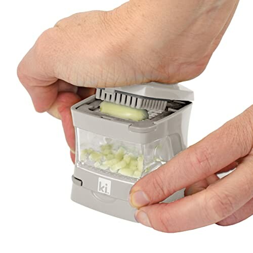 Hand using a garlic chopper with diced garlic pieces.
