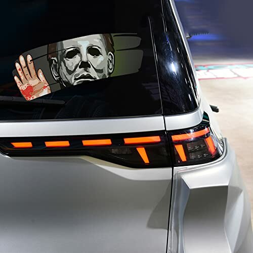 Car window with a horror-themed sticker of a masked figure and bloody handprint.