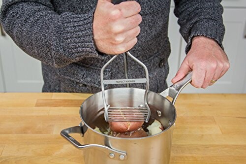 Person mashing potatoes in a pot with a hand masher.