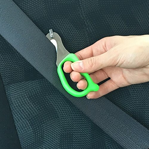 Hand holding a green seatbelt cutter against a car seatbelt.