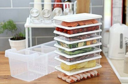 Stacked transparent food storage containers with various foods inside on a kitchen counter.