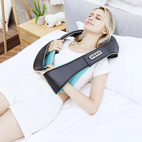 Woman lying on bed using a neck and shoulder massager.