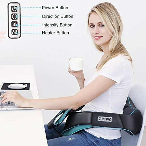 Woman sitting with a massage belt and a cup of coffee, using a laptop.