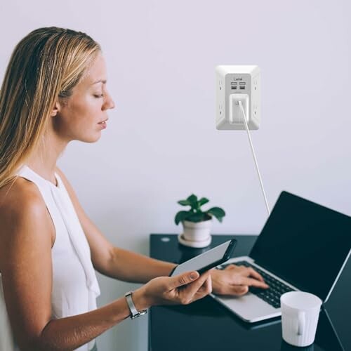 Woman using smartphone and laptop at desk